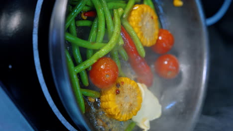 fresh vegetables are being fried on the frying pan. soy sauce is poured to the dish. close up. vertical view.