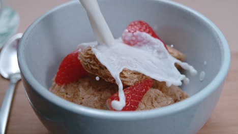 verter leche dinámica en un tazón de cereales para el desayuno y fresas