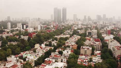 Heavy-fog-covering-skyscrapers-of-Mexico-city,-aerial-fly-view-over-suburbs
