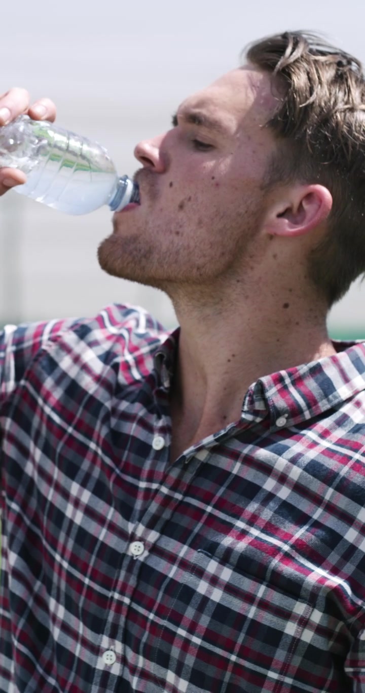 Young Farmer Refreshing Himself with Water in a Greenhouse