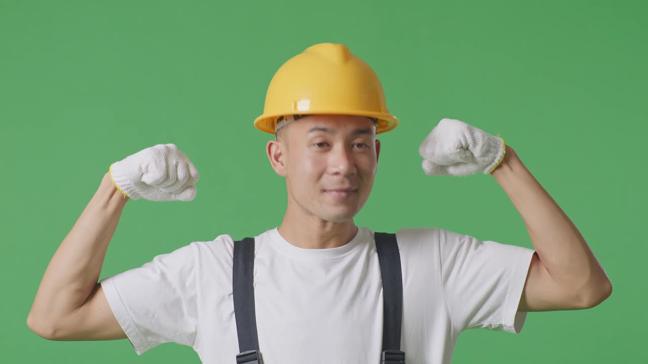 Close Up Of Asian Man Painter Wearing Safety Helmet Smiling And Flexing His Bicep While Standing In The Green Screen Background Studio