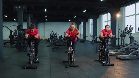 Group-of-girls-performs-aerobic-training-workout-cardio-routine-on-bike-simulators,-cycle-training