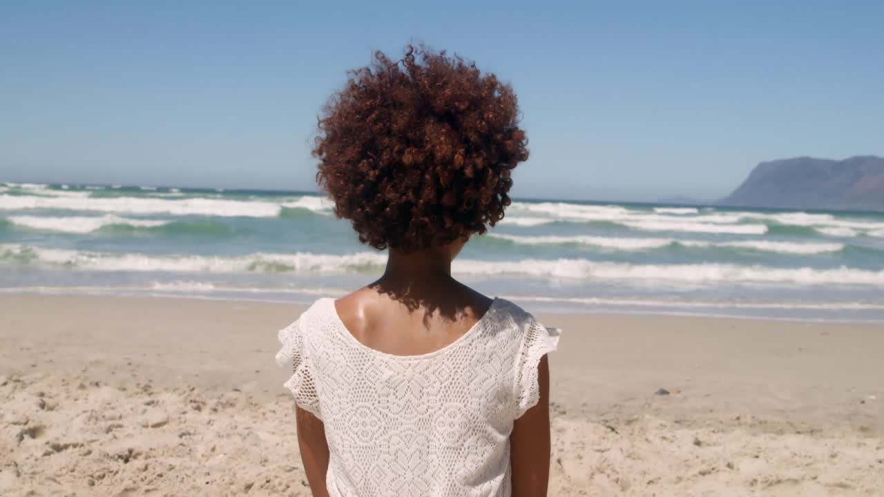 vista trasera de una joven mujer afroamericana relajándose en la playa bajo el sol 4k