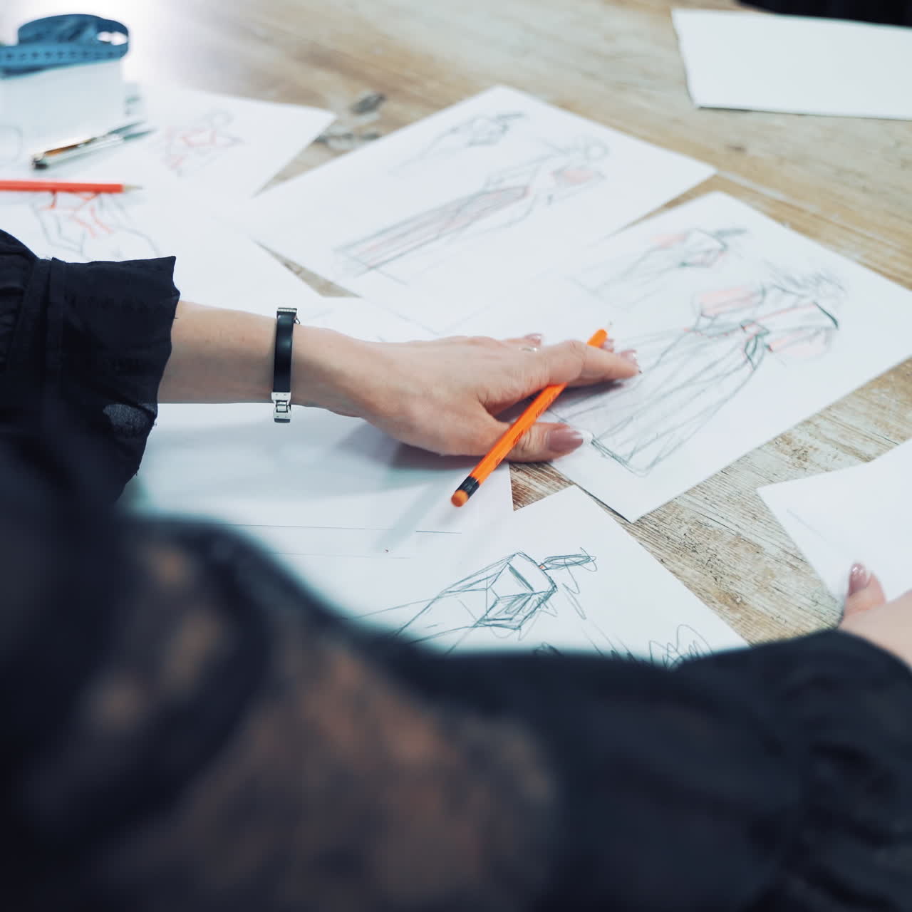 Fashion designer is looking at different sketches and throws away unsuitable one. Workplace of a dressmaker with many drawings of modern dresses written on papers on the table.