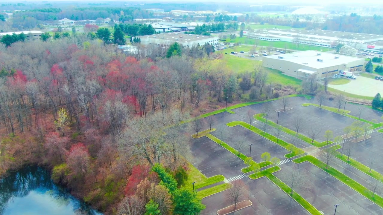 Ripresa con drone che avanza e si inclina verso l'alto, rivelando un'area di parcheggio industriale durante un pomeriggio primaverile a Windsor, Connecticut.