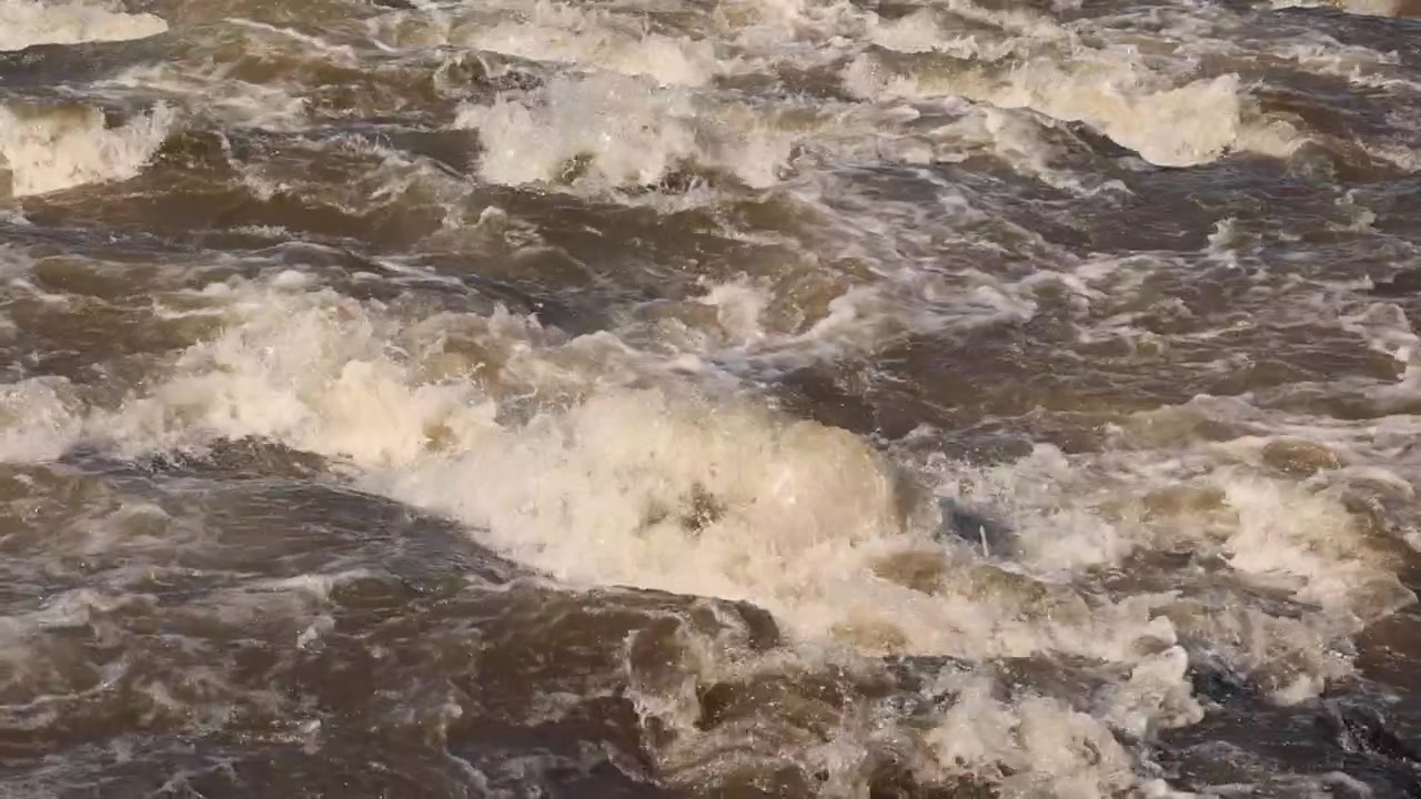 Dettaglio in slow motion prolungato: Rapida di acque bianche di fiume fangoso durante un'alluvione stagionale.