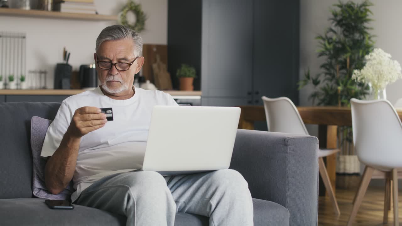Uomo anziano caucasico seduto sul divano che fa acquisti online con carta di credito