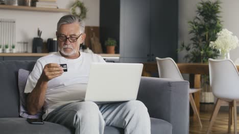 senior caucasian man sitting at couch and make shopping online with credit card.