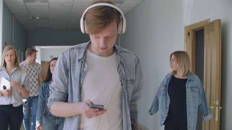 a young man in headphones walks along the inversion corridor listens to music and does not pay attention to people. it is in its own world. an introvert walks through the college hall without talking to students and listens to music and writes chat messages