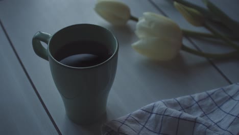 a cup of coffee with white tulip flower on table