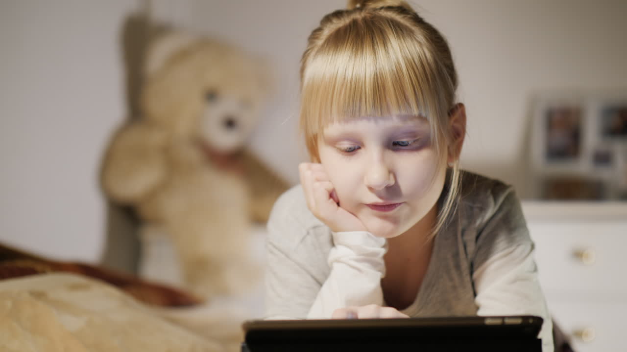 침실이 있는 태블릿을 즐기는 아이의 초상화는 저녁에 침대에 누워 있다