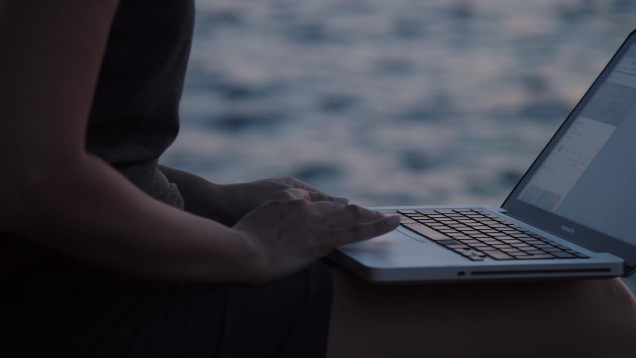 석양에 바다 옆 바위에 앉아 노트북과 소녀 손, 슬로우 모션, 클로즈업