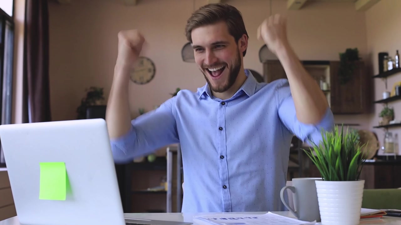 Joven feliz trabajando en el portátil y celebrando el éxito en casa