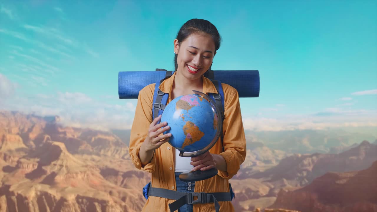 Asian Female Hiker With Mountaineering Backpack Holding World Globe In Her Hands And Smiling To Camera While Traveling At The Top Of Mountain