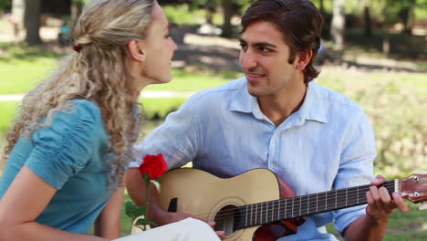 el novio toca la guitarra para su novia mientras ella sostiene una rosa y luego besa