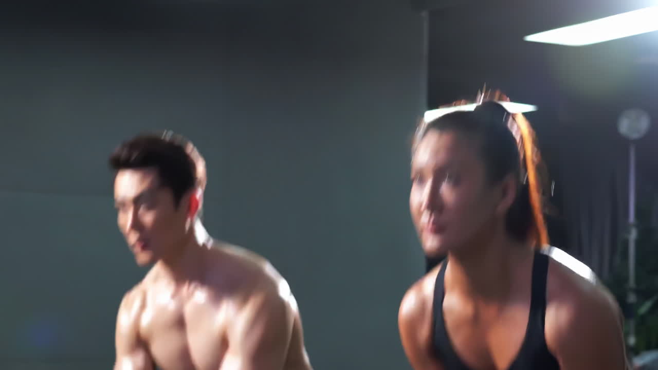 Muscular sportsman sportswear bodybuilder holds dumbbell in hand and does exercises for arm muscles, pumping up biceps in gym fitness with support of crossfit trainer athlete attractive woman.