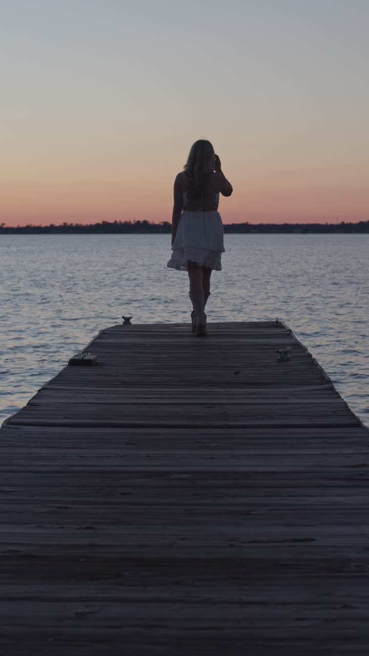 Ripresa al rallentatore di una bella ragazza bionda che cammina lungo un pontile al tramonto