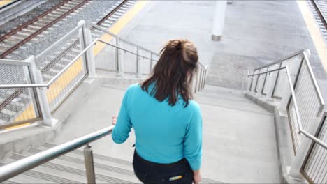 woman in blue walks down the stairs at a train station and shakes her head