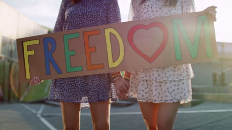 video de dos mujeres de pie con vallas publicitarias y tomadas de la mano