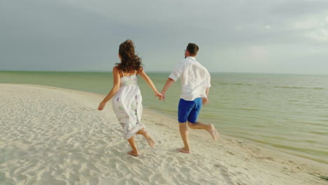 Joven-Pareja-De-Enamorados-En-Ropa-Ligera-Sin-Preocupaciones-Corriendo-En-Una-Playa-Tropical-Limpia