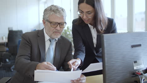 friendly positive female assistant in suit and glasses showing data to her boss