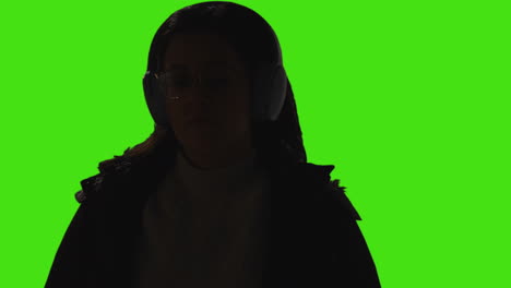 close up of woman wearing wireless headphones streaming music from mobile phone against green screen background