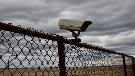 security camera on a rusty fence under a cloudy sky