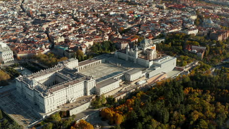 Aerial-view-of-large-historic-Royal-Palace-complex-at-golden-hour.-Colourful-foliage-on-trees-in-park-of-gardens.-Tilt-up-revealing-cityscape.