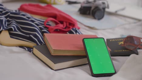 teléfono móvil de pantalla verde con maleta abierta en la cama en casa siendo empacado para las vacaciones de verano 2