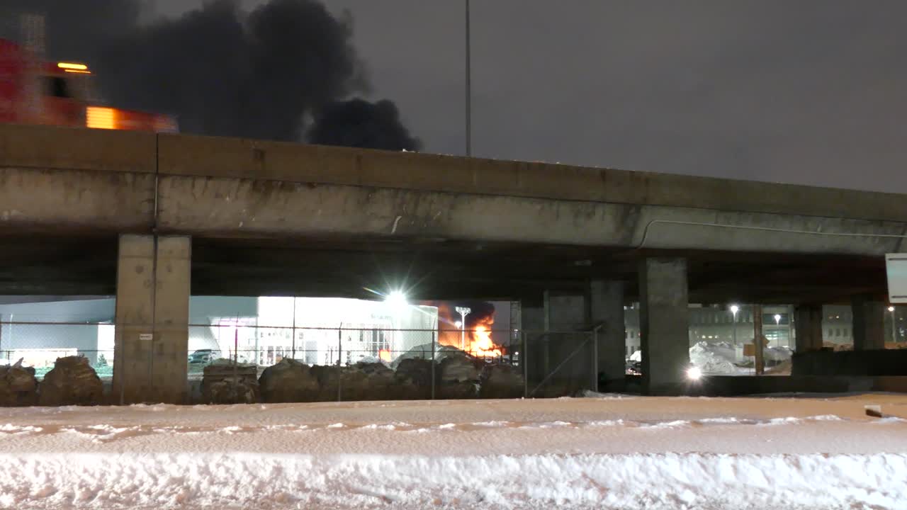 Fire truck crosses bridge as thick black smoke rises from industrial blaze