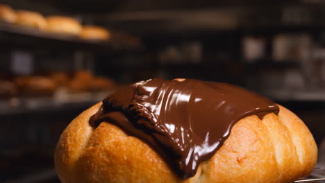 pouring melted chocolate over a fresh baked bun