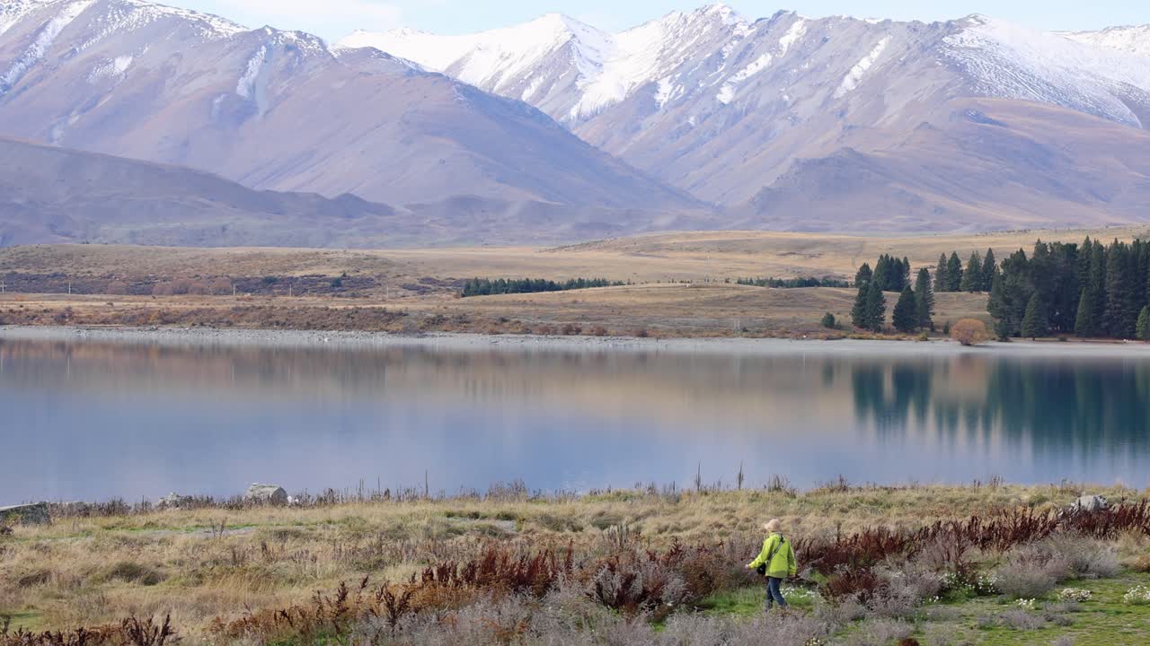 A person in bright clothing jogs along Lake Tekapo, surrounded by mountains and serene waters under clear daylight