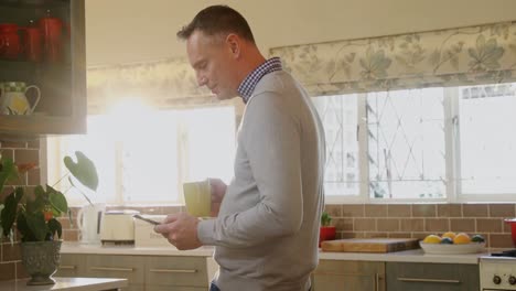 hombre usando teléfono móvil mientras toma café en la cocina 4k
