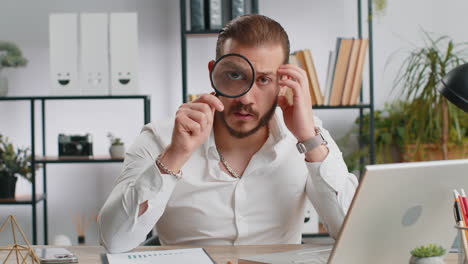 business man holding magnifying glass near face looking with big zoomed eye searching analysing