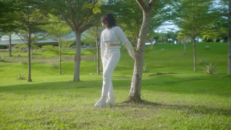 woman in long sleeve crop top and white ripped pants relaxing and standing alone in the park