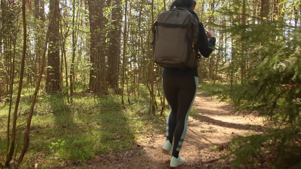 mujer caminando con una mochila de senderismo en el bosque verde de primavera