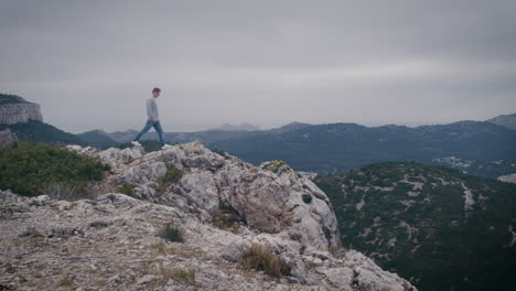 Hiker-walks-on-rocks,-explores-high-mountain-ridges,-looks-at-scenery