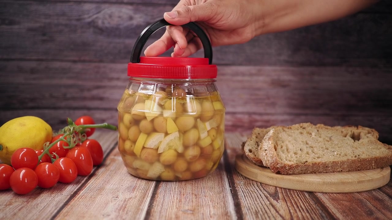 Mano levantando un tarro de aceitunas encurtidas de una mesa de madera