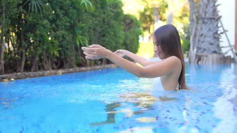 Mujer-Exótica-Sexy-En-Traje-De-Baño-Divirtiéndose-Con-Agua-En-La-Piscina-Del-Resort-Tropical,-Cámara-Lenta