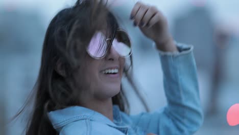 una mujer joven posando con grandes gafas de sol redondas y divertidas, el viento soplando el cabello