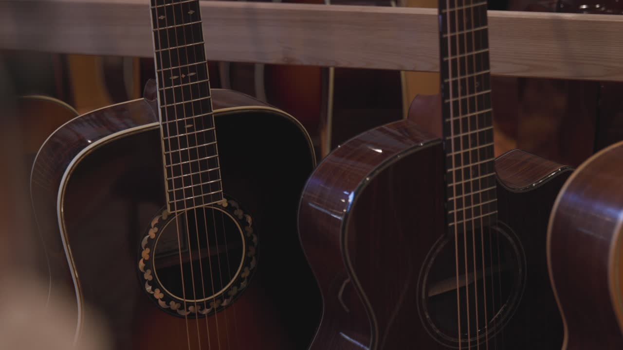 Handheld slow motion footage panning across the bodies of a bunch of acoustic guitars in a store.