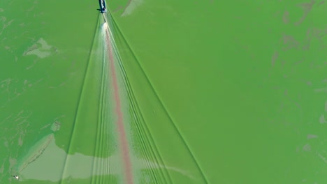 static aerial view boat going through low algae covered water on the tonle sap during rainy season, with extreme low water table, cambodia