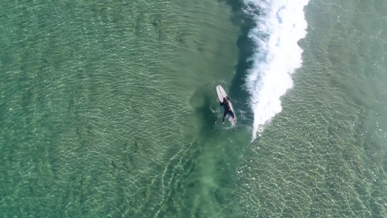 Un uomo che rema in mare aperto sulla sua tavola da surf in acque limpide in una luminosa giornata estiva
