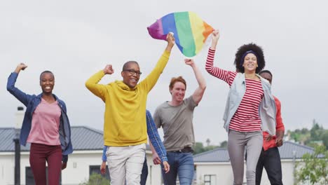 Happy group of diverse male and female protesters walking with rainbow flag