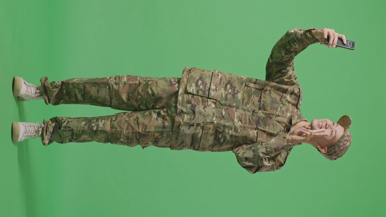 Full Body Of Asian Man Soldier Using Smartphone Taking Picture While Standing In The Green Screen Background Studio
