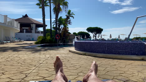 a view of a man's feet, a man lies on a lounger by the pool