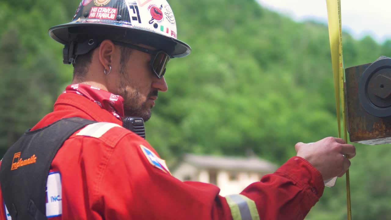 Worker in red uniform rigging bridge construction equipment at a site in Tende, South of France