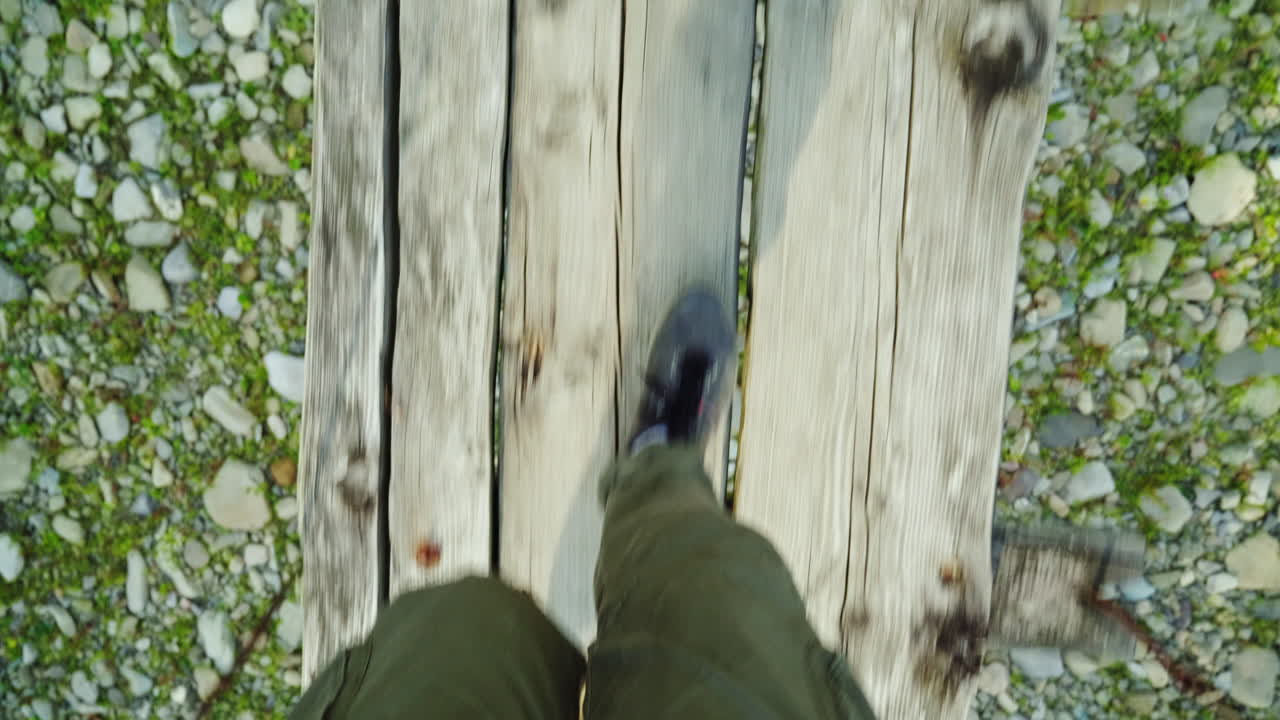 한 남자의 발이 산 강 위험과 모험가 위의 좁은 나무 다리를 따라 걷고 있다