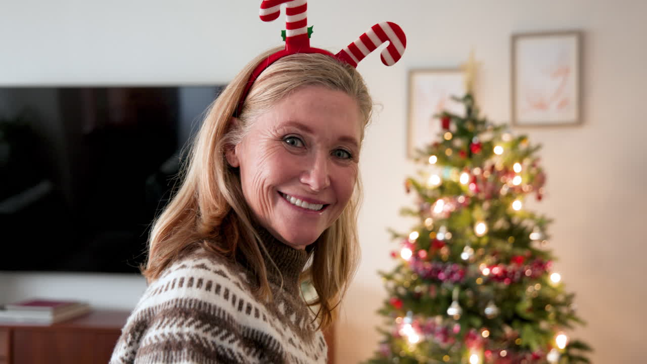 Smiling senior woman wearing festive headband near decorated Christmas tree at home