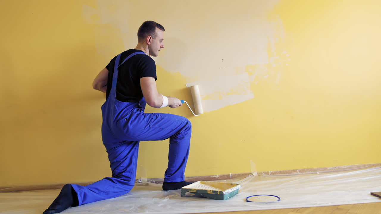 Young man painting wall with roller brush while renovating his apartment. Repair, building and home concept.